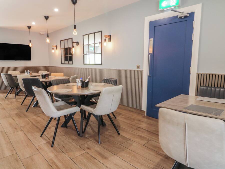 Un comedor moderno con mesas y sillas redondas, una puerta azul e iluminación colgante.