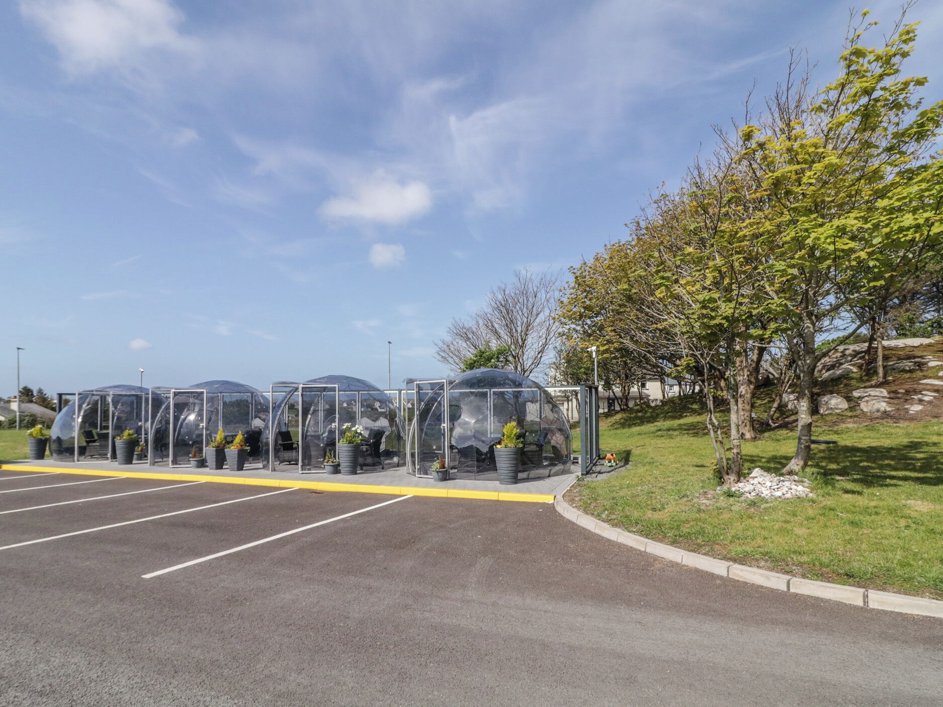 A parking lot with clear, transparent structures housing potted plants.