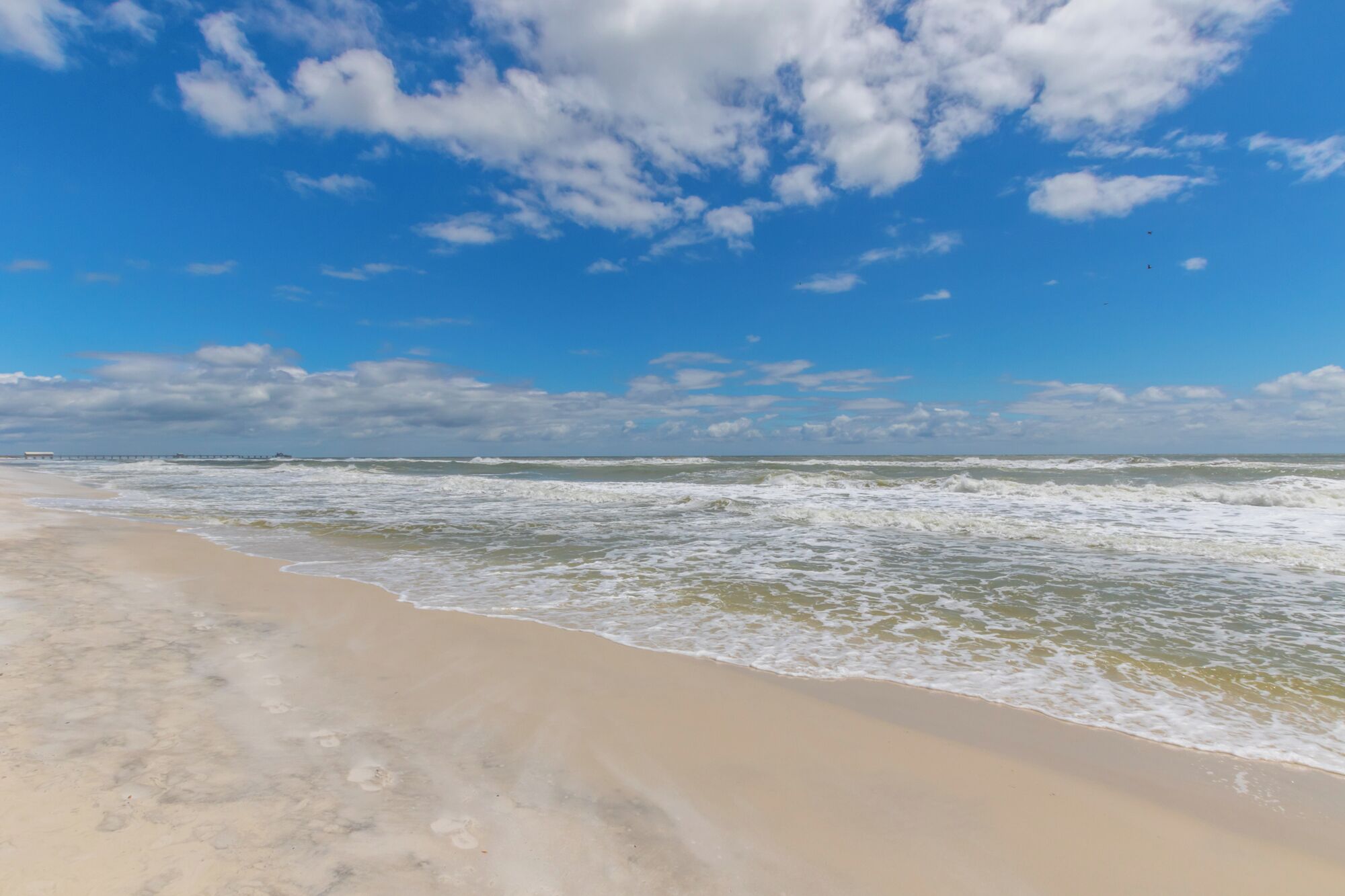 A beach with waves, a clear sky, and a distant pier.