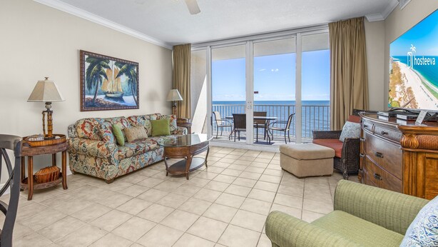 A spacious living room with a sofa, a coffee table, and a TV on a balcony overlooking the sea. - San Carlos Unit 607 (Gulf Shores)