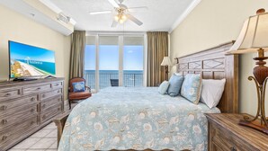 A bedroom with a large bed, a television, a ceiling fan, and a view of the ocean. - San Carlos Unit 607 (Gulf Shores)