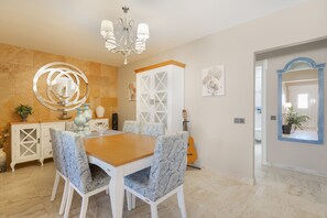 A dining area with a wooden table, patterned chairs, a chandelier, a guitar, and a mirror with a blue frame.