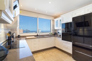 A modern kitchen with white cabinets, a black refrigerator, and a large window offering a view of the sea.