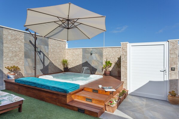 A hot tub with steps, a wooden deck, a white door, and potted plants.