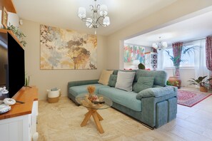A living room with a sofa, a glass coffee table, a chandelier, and artwork on the walls.