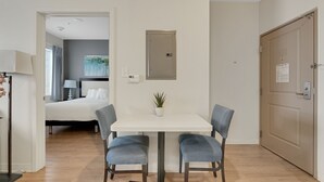 A hotel room with a bed, a desk with a lamp, a small potted plant, and a door with a sign. - Simplicity At the Rim 1107 I Spacious 1 Bed 1 Bth (San Antonio)