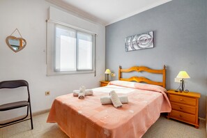 Ein Schlafzimmer mit einem Bett, zwei Nachttischlampen, einem Nachttisch, einem Sessel, einem Fenster und einem Wandbild.
