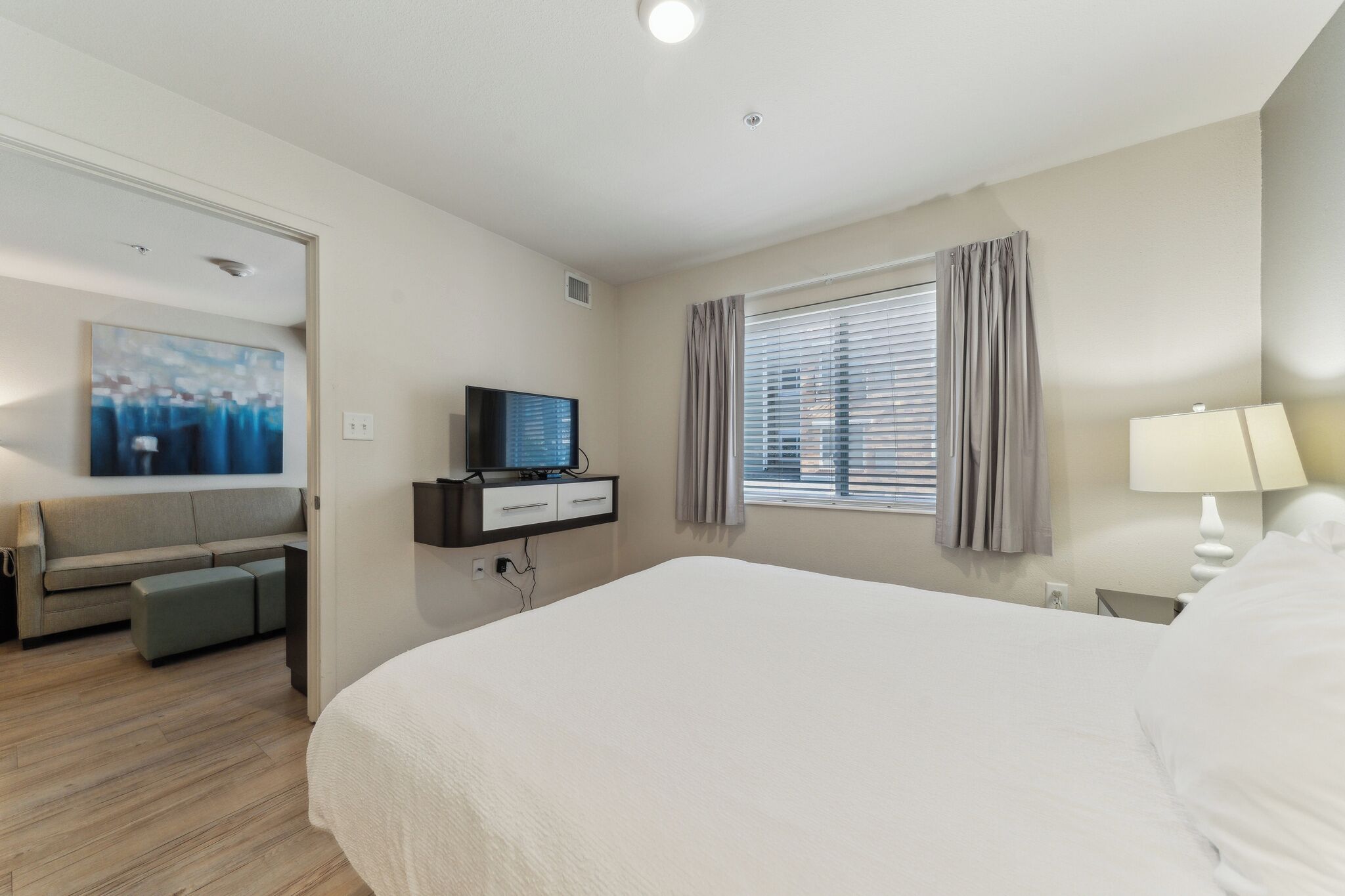 A hotel room with a large bed, a TV on a stand, a sofa, and a painting on the wall.