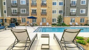 Un espace aménagé au bord de la piscine, avec des chaises longues et une petite table, entouré d’un immeuble à plusieurs étages doté de balcons.