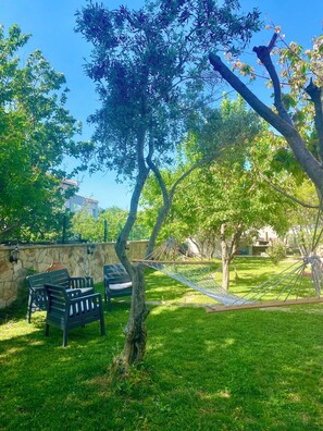 A grassy outdoor area with a hammock, a stone wall, and a bench. - ADAHAN APART (Gokceada)