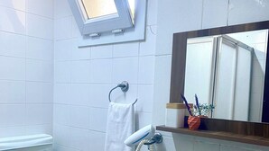 Un baño con inodoro, lavamanos y ventana sobre el lavabo.
