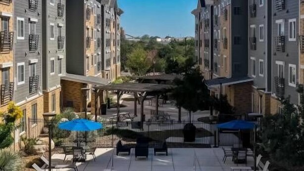 Um complexo de apartamentos moderno com piscina central, área de estar ao ar livre e vista desobstruída da região.