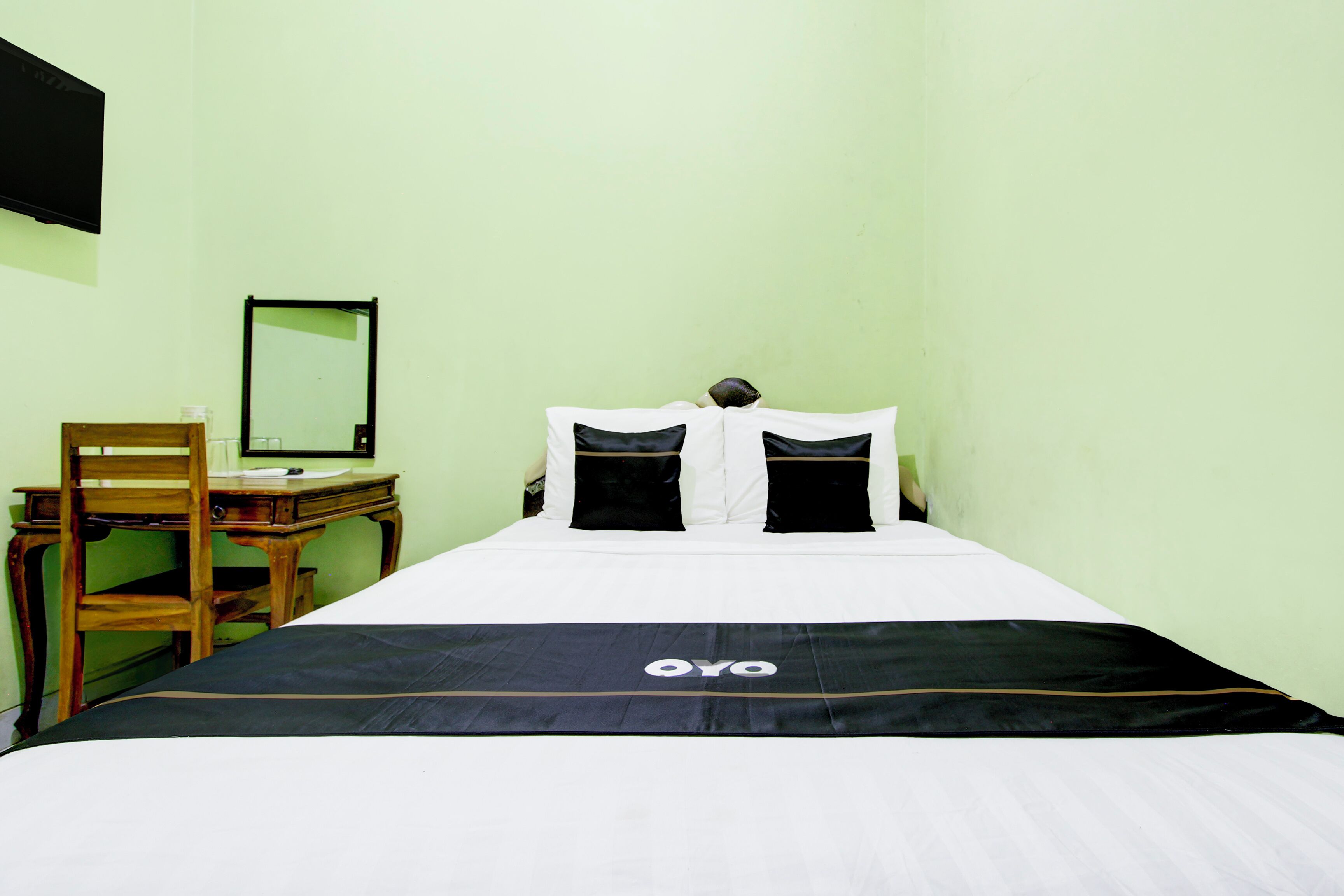 A single bed with a black and white bedspread, a wooden chair, and a desk with a mirror.