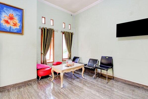 Una habitación con una mesa de madera, dos sillas rojas, dos sillas negras, un cuadro de flores y un televisor en la pared.