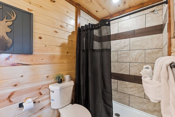 Un baño de cabaña de madera con cortina de ducha, un inodoro y un perchero para toallas.
