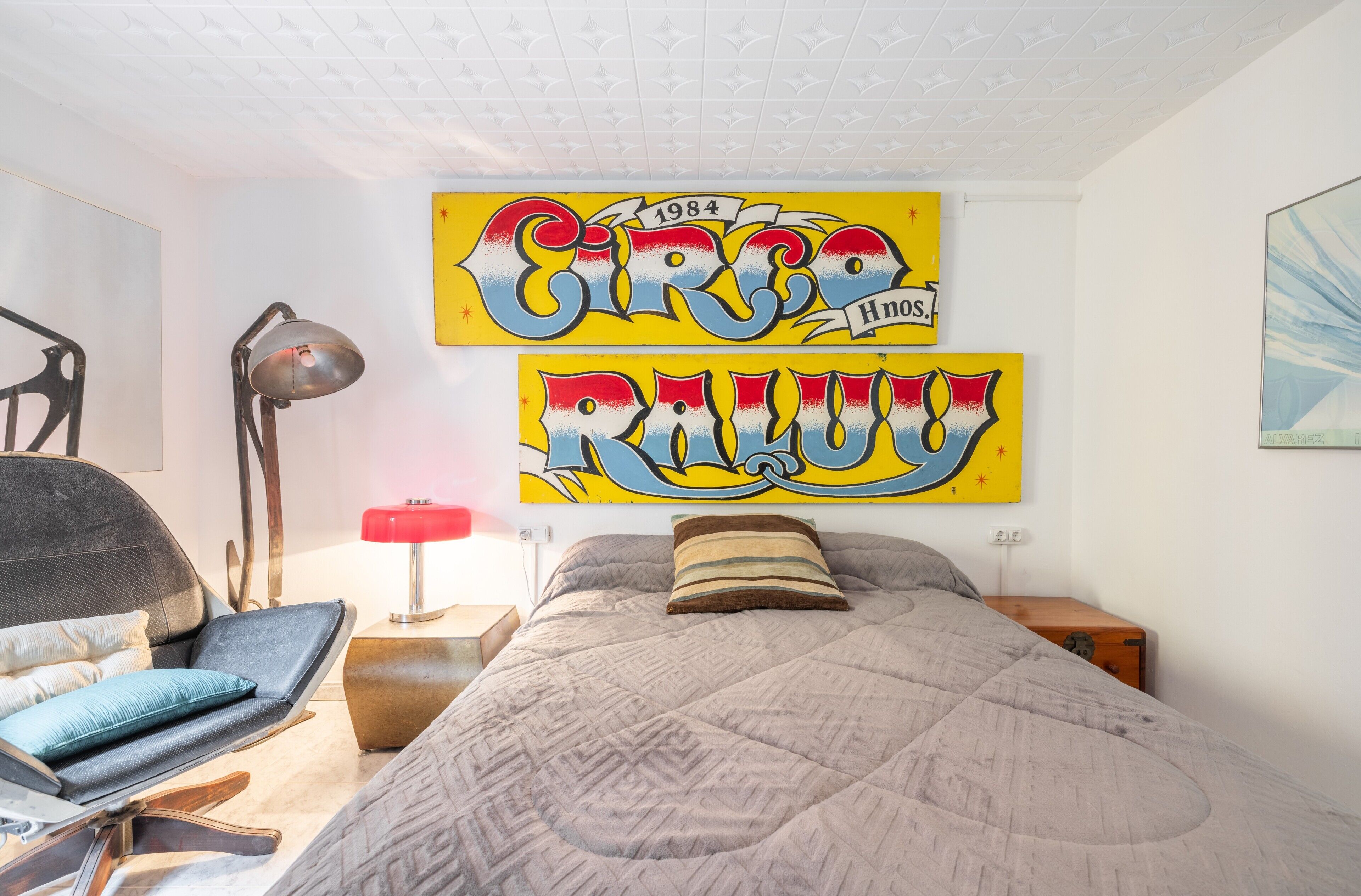 Un dormitorio con una cama, una silla, una lámpara y dos obras de arte grandes en la pared.