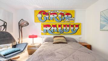 Un dormitorio con una cama, una silla, una lámpara y dos obras de arte grandes en la pared.