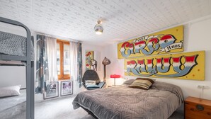 Un dormitorio con una cama nido, una cama grande, un escritorio, una silla y obras de arte en las paredes.