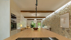 Une cuisine moderne dotée de fours encastrés, d’une table à manger en bois et d’un mur en pierre.