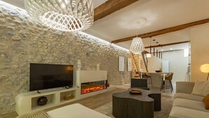 Un salon moderne avec un mur en pierre, une cheminée, un téléviseur à écran plat et un coin repas agrémenté d’une échelle.