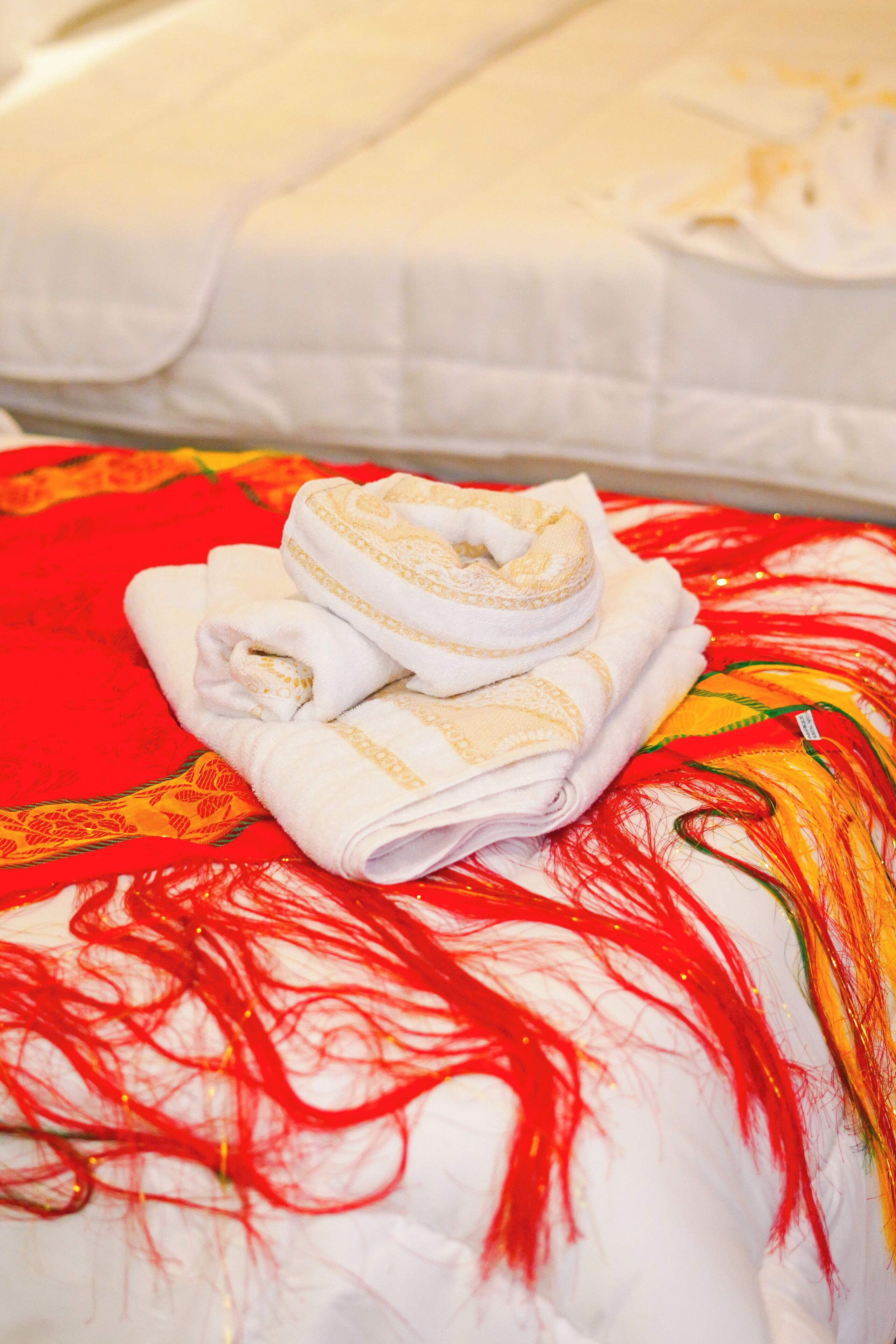 Una toalla doblada con cuidado sobre una cama con una colcha de rayas rojas y amarillas.