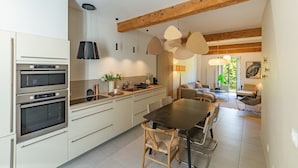 Eine moderne Küche mit Einbauöfen, ein Essbereich mit Tisch und Stühlen sowie ein Wohnzimmer mit Sofa.