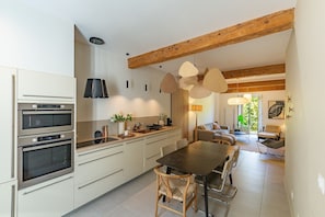 A modern kitchen with built-in ovens, a dining area with a table and chairs, and a living room with a sofa.