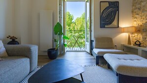 Ein Zimmer mit einer Couch, einem Tisch, einer Zimmerpflanze, einem Balkon mit Aussicht und einer Lampe.