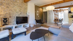 Ein Wohnzimmer mit Steinwand, einem Flachbildfernseher, einer Couch, einem Sessel und einem Essbereich im Hintergrund.