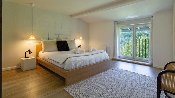 Ein Schlafzimmer mit Bett, Nachttischlampen, einem Nachttisch, einem großen Fenster mit Blick und Holzboden.