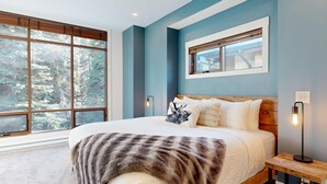 Un dormitorio con una cama grande, vistas a árboles por la ventana y una mesita de noche con una lámpara.