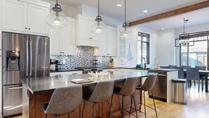 Una cocina moderna con electrodomésticos de acero inoxidable, una isla grande con taburetes de bar e iluminación colgante.