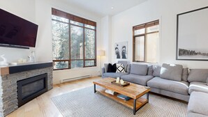 Una sala de estar moderna con chimenea, ventanas amplias, un sofá gris y un televisor de pantalla plana.