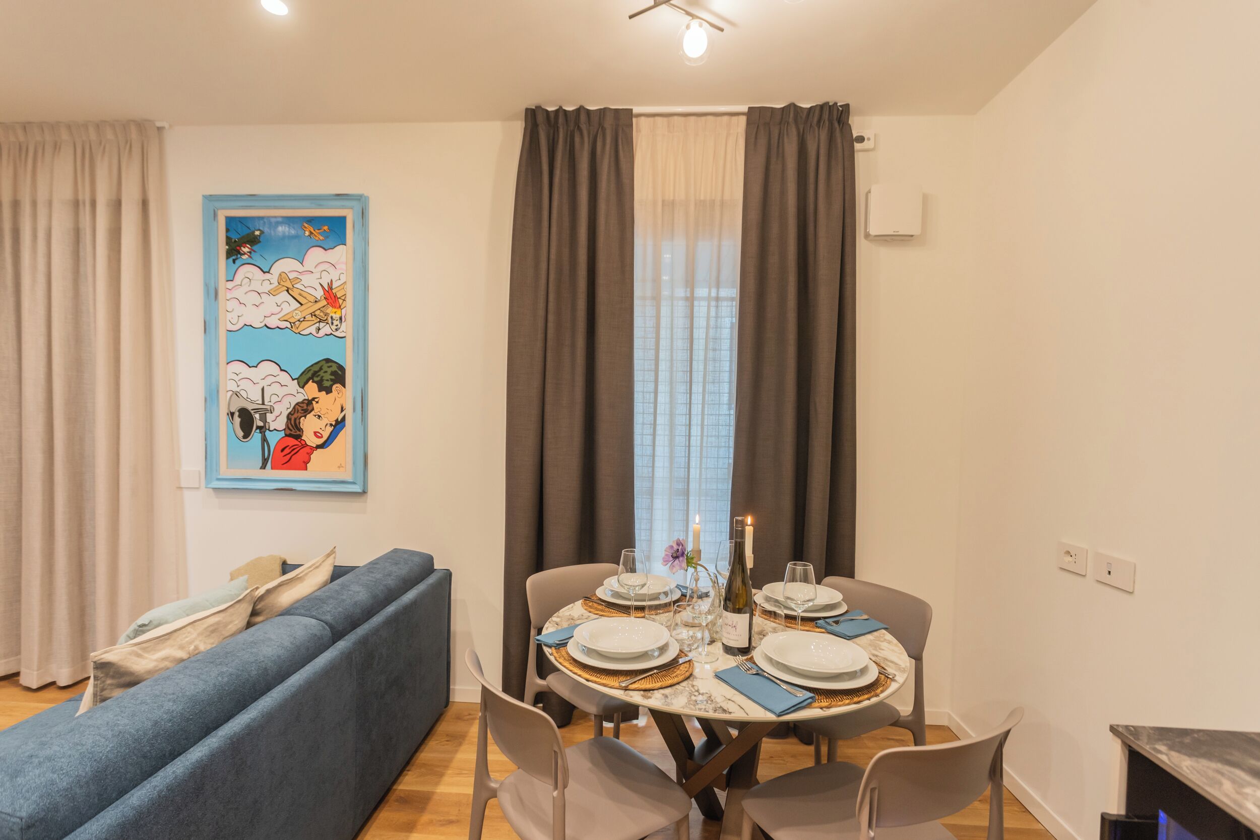 Un coin repas avec une table dressée pour quatre personnes, un canapé bleu et un tableau accroché au mur.