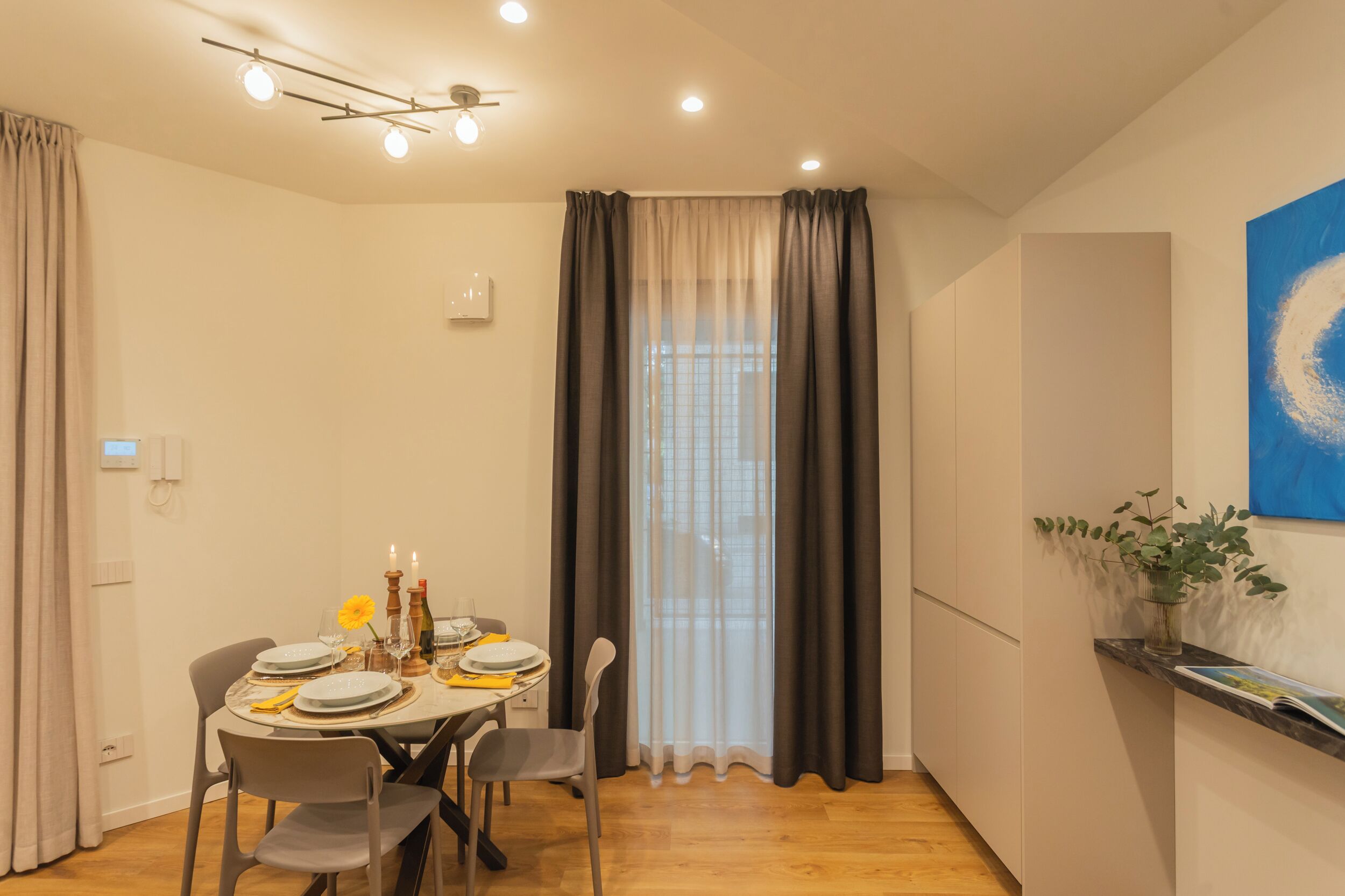 A dining area with a table set for four, a ceiling fan, and a large window with curtains.
