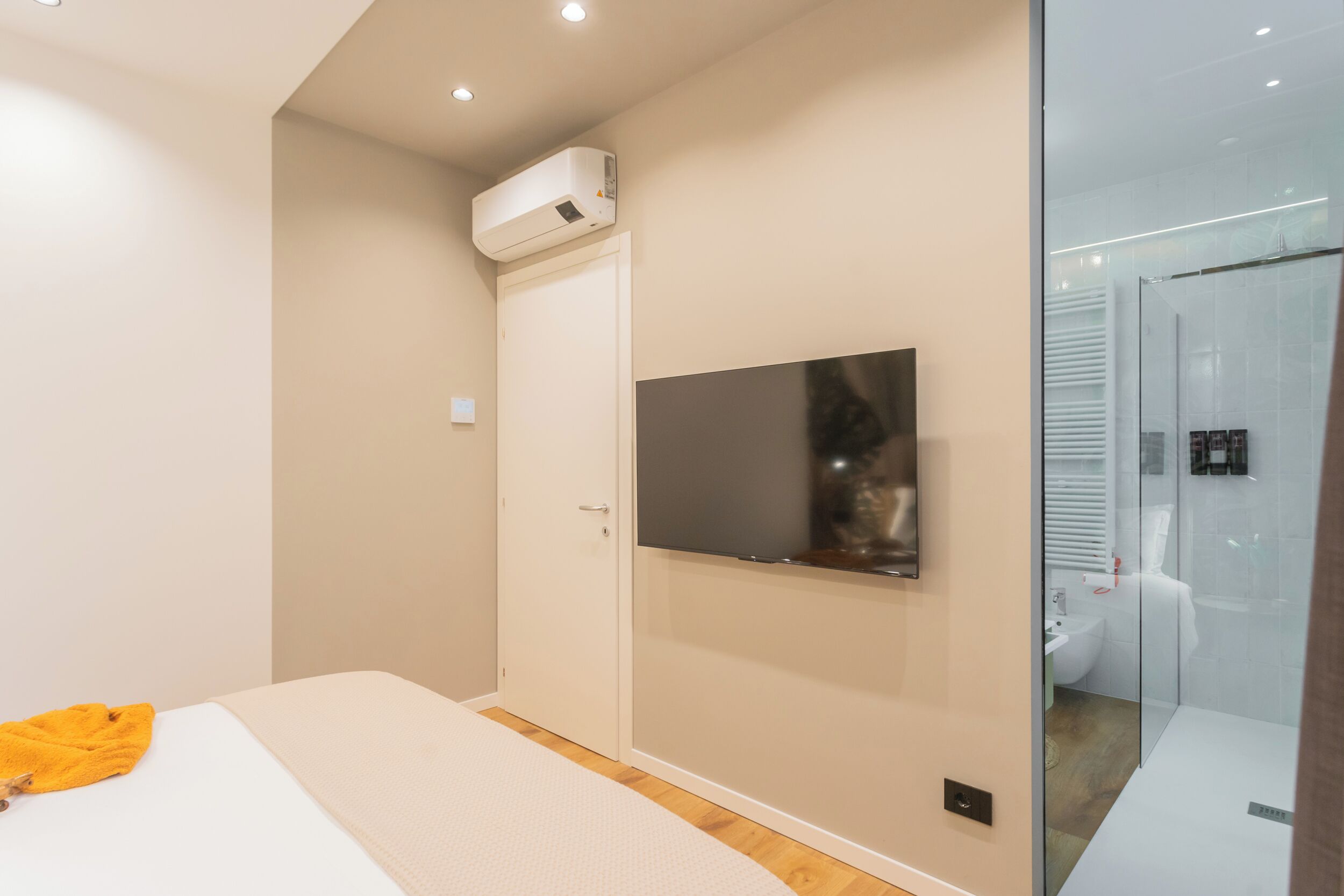 A modern bedroom with a bed, a mounted TV, and a glass shower enclosure.