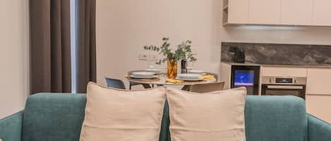A teal sofa with two pillows, a magazine, and a small table with a plant and a vase.