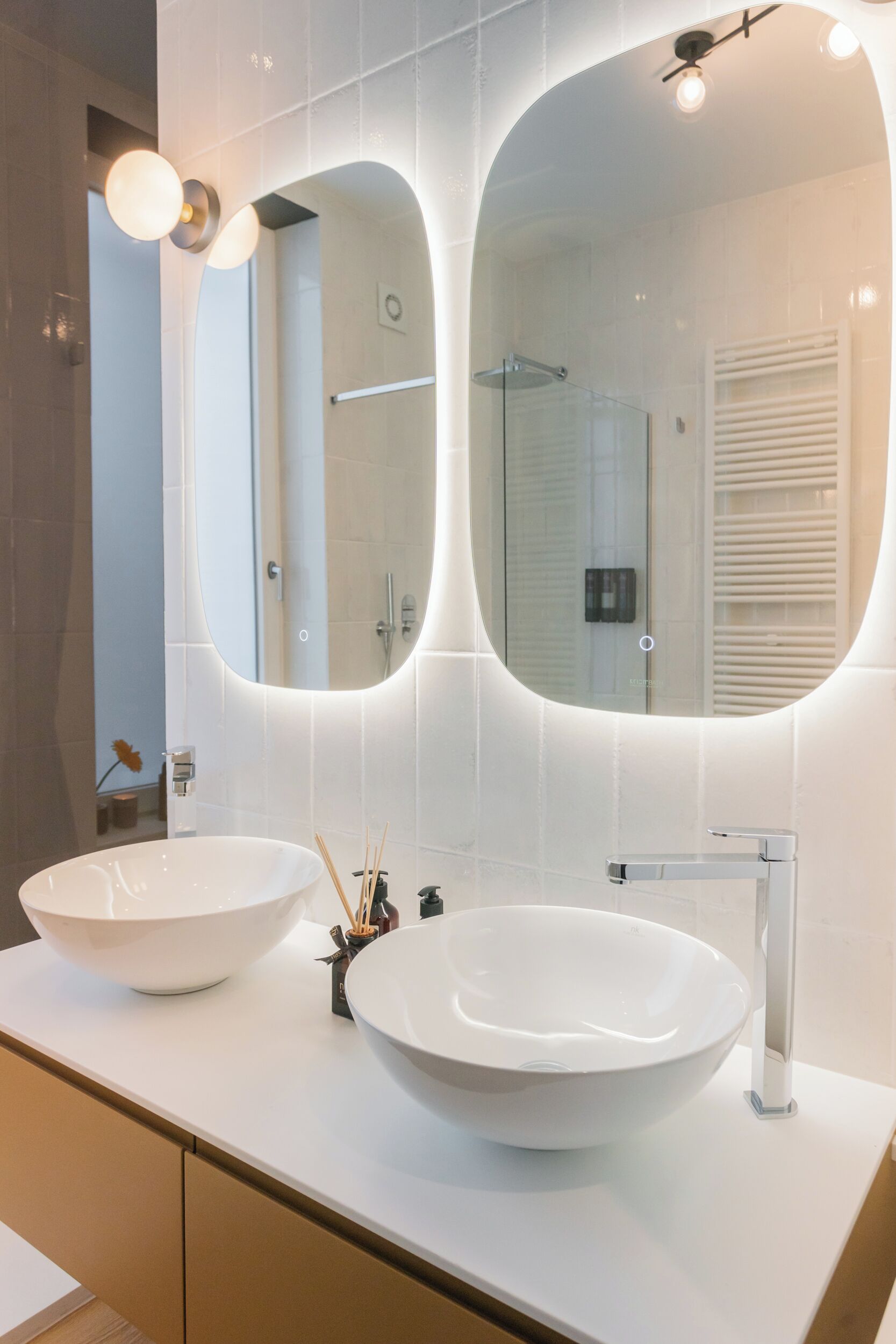 Une salle de bain moderne avec deux grands lavabos blancs, un grand miroir et un espace douche.