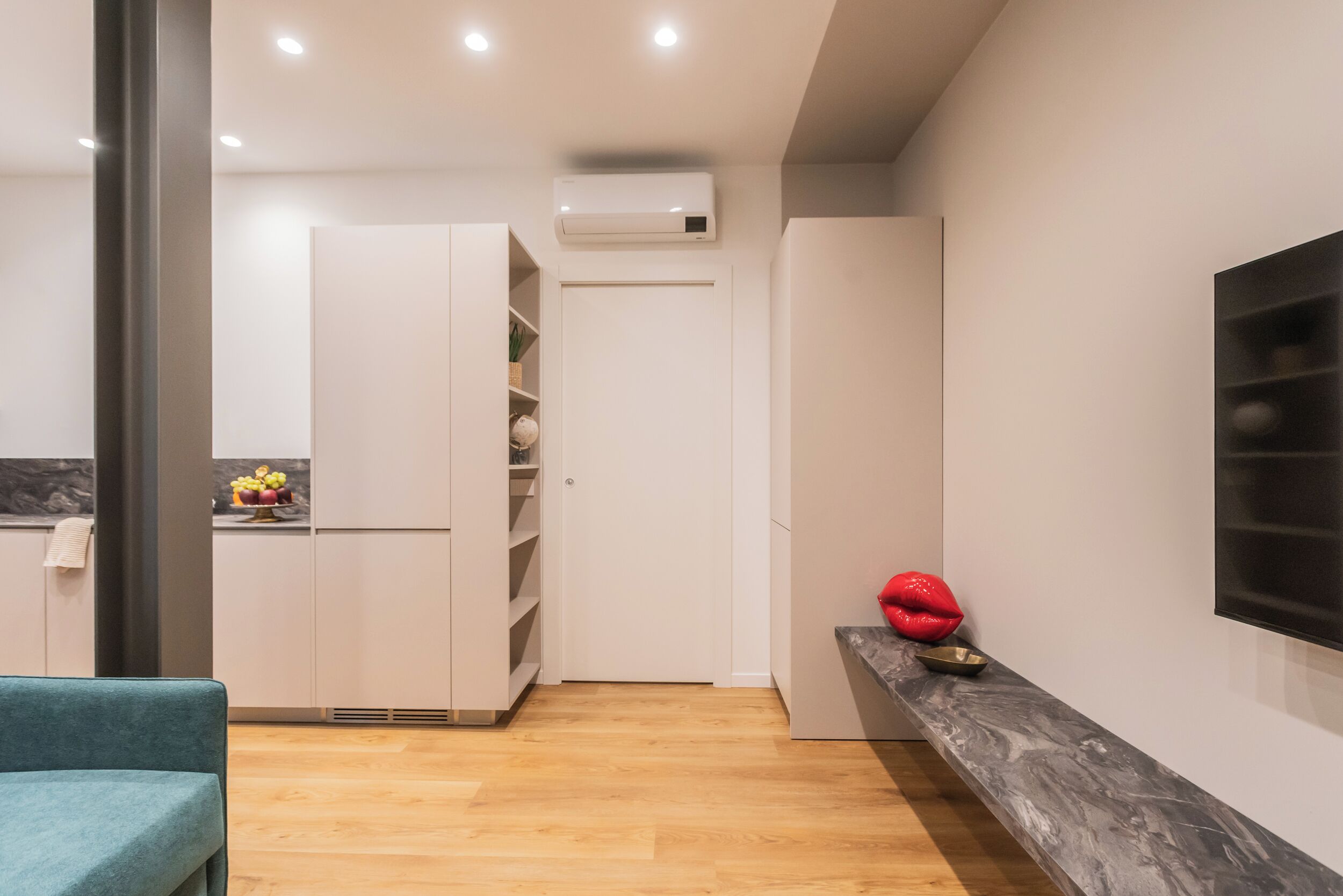 A modern kitchen with white cabinets, a wooden floor, and a built-in air conditioning unit.