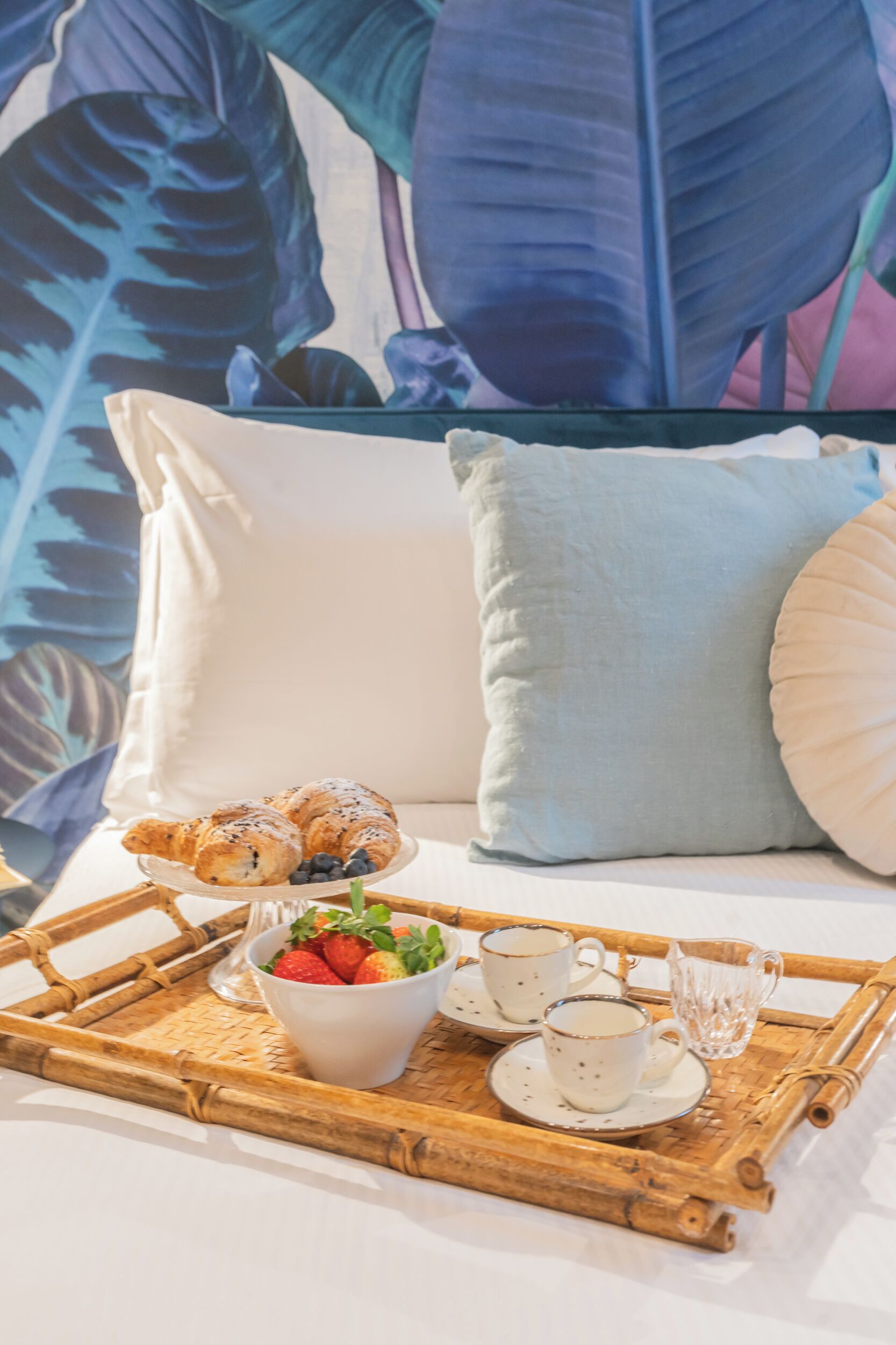 A bed with pillows and a tray with croissants, strawberries, and cups.