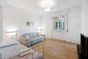 A bedroom with a bed, a sofa, a TV, and a window.