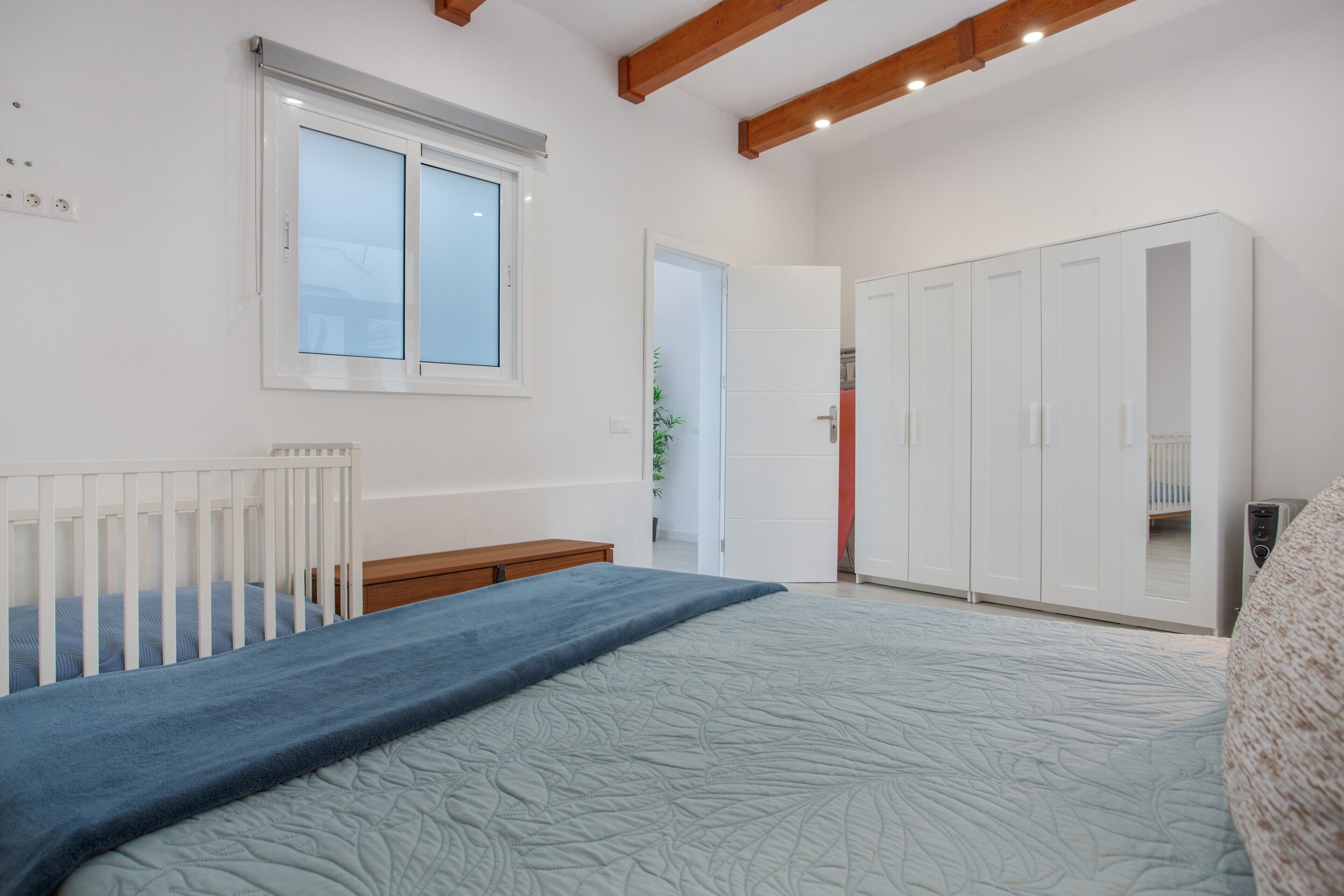 Ein Schlafzimmer mit einem Bett, einem Babybett, einem Kleiderschrank und einem Fenster.