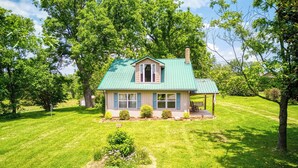 A single-story house with a green roof, a porch with a bench, and a well-maintained lawn.
