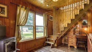 A wooden cabin interior with a staircase, a fireplace, and a window overlooking a garden. - Valley View Farmhouse- Hot Tub, $560 Tickets per Paid Day (Sevierville)