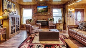 A cozy cabin interior with a fireplace, leather furniture, and wooden walls. - Valley View Farmhouse- Hot Tub, $560 Tickets per Paid Day (Sevierville)