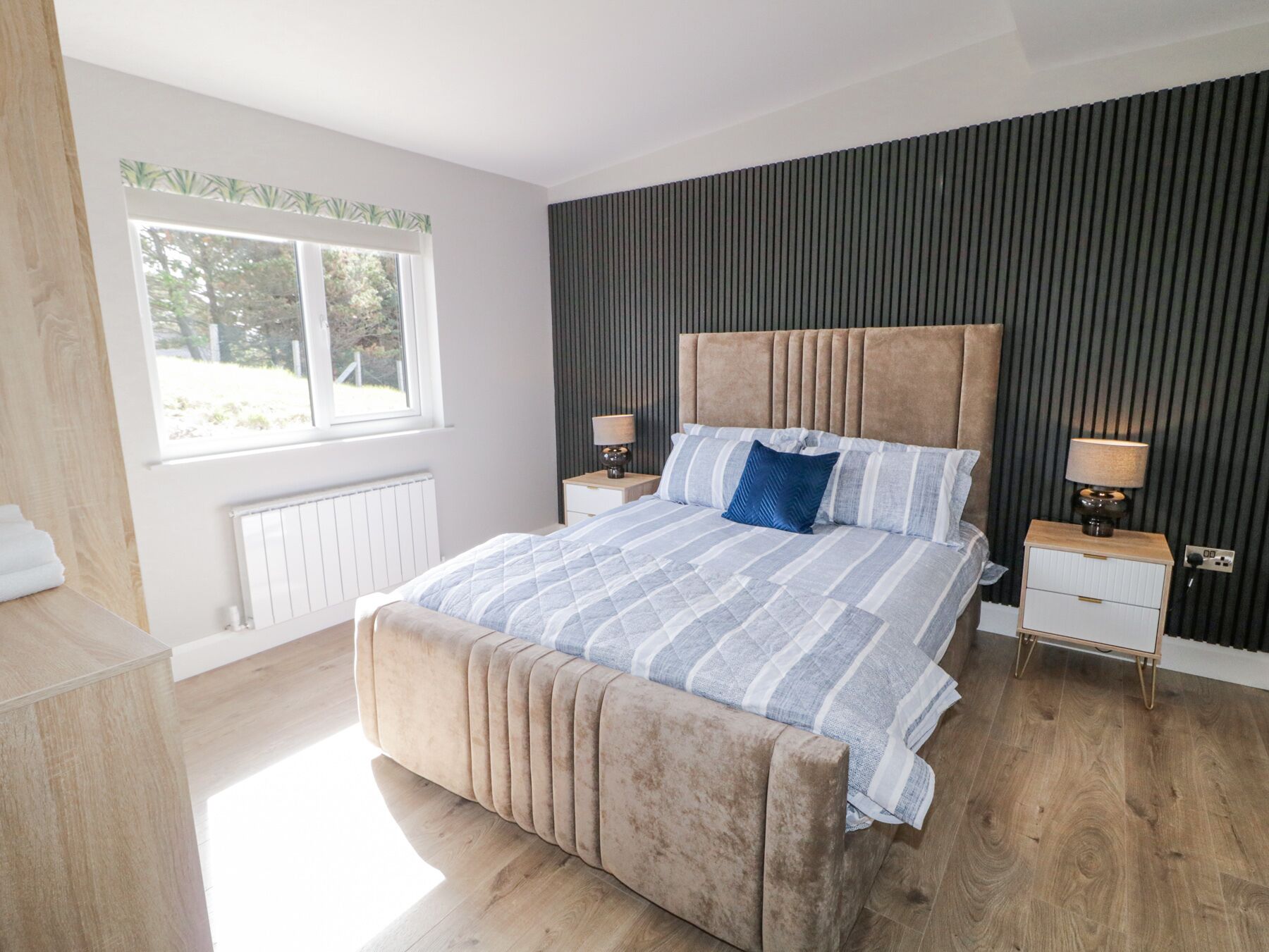 A bedroom with a large bed, two bedside tables, a window, and a radiator.