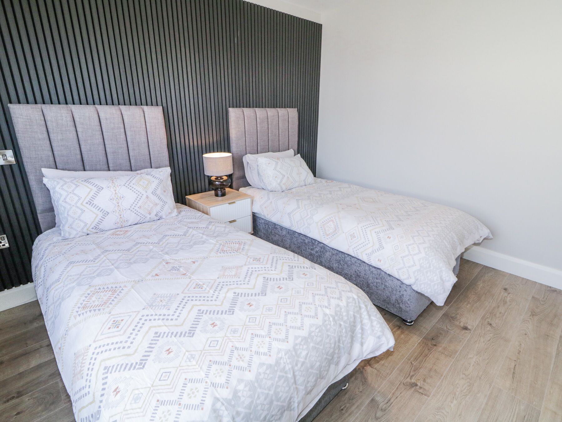 A double bed with a geometric patterned duvet, a bedside table with a lamp, and a headboard with vertical slats.
