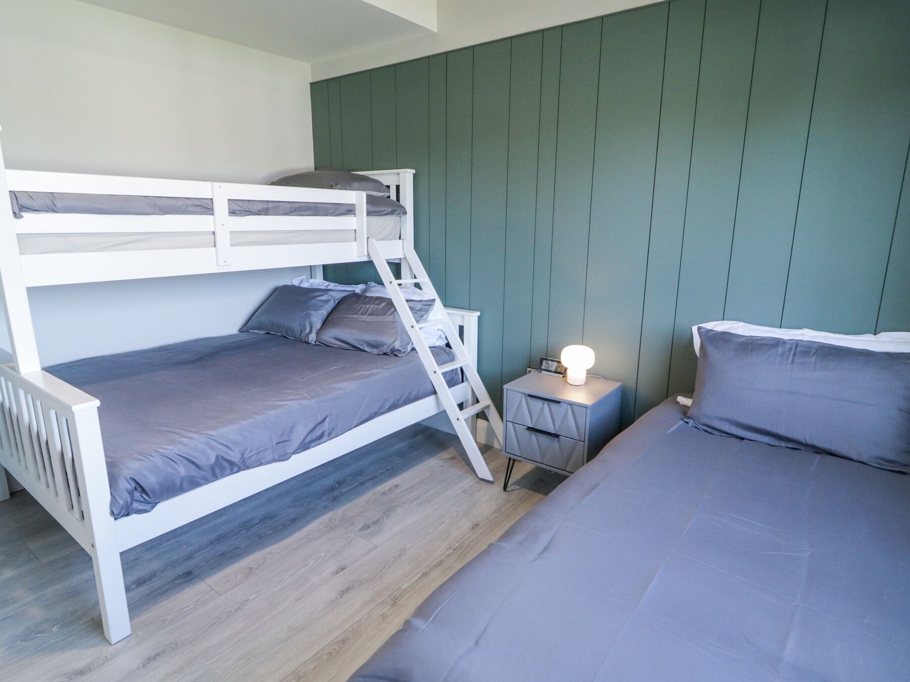 A bunk bed room with a ladder, a bedside table with a lamp, and a nightstand.