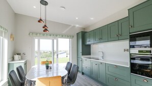 A modern kitchen with green cabinets, a central island, and a dining area with chairs. - Number 3 Villa - The View (Bunbeg)