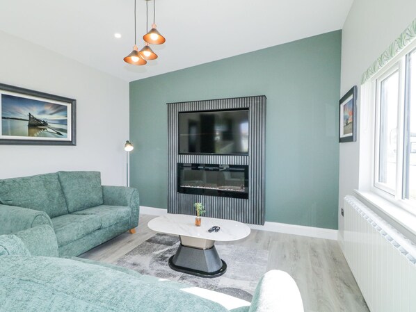 Un salon moderne avec un canapé de couleur turquoise, une table basse ronde et un téléviseur à écran plat fixé au mur, lequel est décoré de motifs à rayures verticales.
